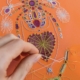 Au Musée de la Toile de Jouy, une main brode du fil blanc sur un tissu orange, l'ornant de motifs cousus colorés, dont des araignées, des toiles et des cœurs. - Musée de la Toile de Jouy