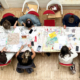 Au musée de la Toile de Jouy, un groupe de personnes est assis autour d'une table couverte de fournitures d'écriture et d'art colorées, travaillant sur des projets créatifs. La photo, prise du dessus, montre des outils, du papier et des cahiers éparpillés sur la table. - Musée de la Toile de Jouy