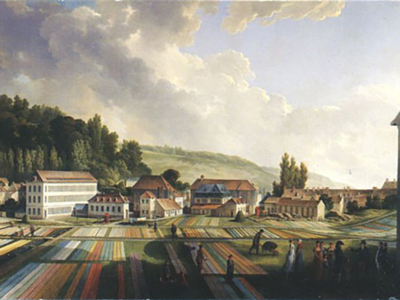 Scène de village du XIXe siècle avec des personnes travaillant sur des bandes de tissu colorées disposées dans des champs, rappelant les motifs vus au musée de la Toile de Jouy, entourées de maisons, d'arbres et de collines sous un ciel partiellement nuageux. - Musée de la Toile de Jouy