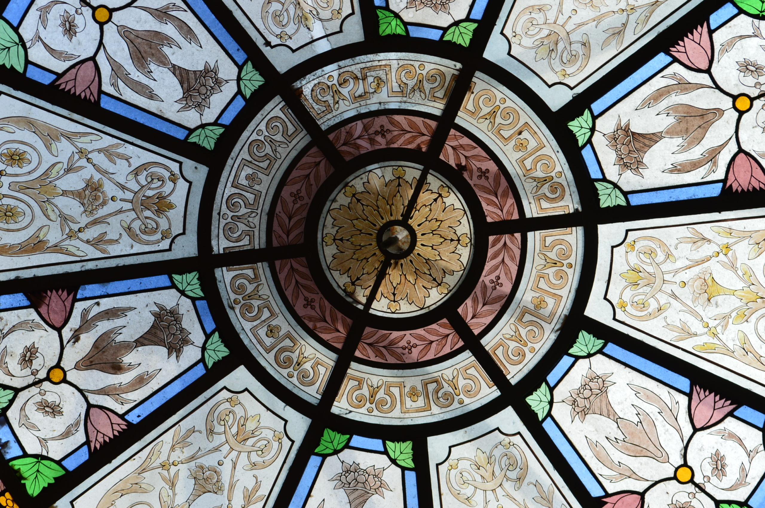 Le plafond circulaire en vitrail du musée de la Toile de Jouy présente des motifs floraux et géométriques en bleu, vert, rose et crème, divisés en sections décoratives rayonnant à partir d'un médaillon floral central. - Musée de la Toile de Jouy