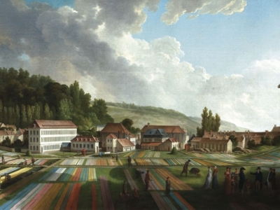 Un paysage pittoresque montrant des bandes de tissu colorées qui sèchent dans les champs, des gens qui marchent et parlent, et des bâtiments près d'une colline boisée sous un ciel partiellement nuageux, évoque le charme paisible et pastoral du musée de la Toile de Jouy. - Musée de la Toile de Jouy