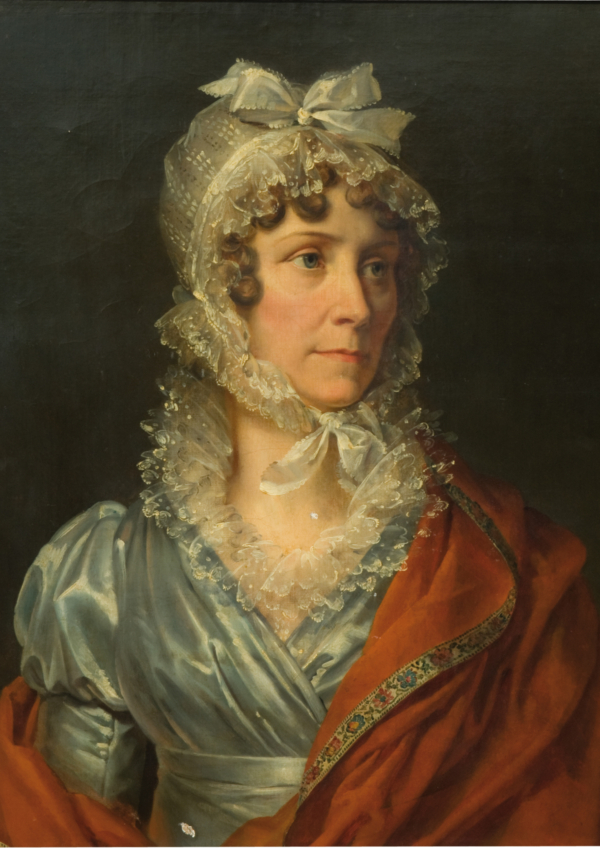 Une femme vêtue d'une robe bleu clair à manches bouffantes et d'un châle rouge, coiffée d'un bonnet en dentelle avec un nœud, regarde vers la gauche sur un fond sombre dans ce portrait classique exposé au musée de la Toile de Jouy. - Musée de la Toile de Jouy