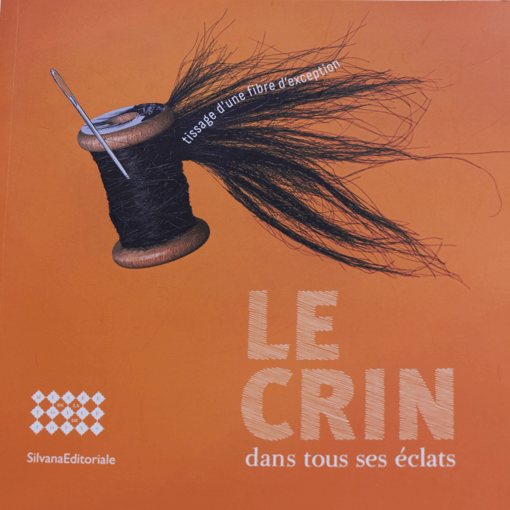 Une couverture orange avec une bobine de crin foncé, une aiguille à coudre et le texte "tissé d'une fibre d'exception, LE CRIN dans tous ses éclats". Les logos du Musée de la Toile de Jouy et de Silvana Editoriale apparaissent en bas à gauche. - Musée de la Toile de Jouy