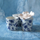 Trois tasses en porcelaine blanche à motifs floraux bleus sont présentées sur un tissu bleu à motifs de dentelle, évoquant l'élégance raffinée du musée de la Toile de Jouy. L'une des tasses est surmontée d'une délicate fleur blanche. - Musée de la Toile de Jouy