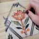 Une main utilise un petit outil pour guider un fil coloré autour de clous sur une planche en bois, créant ainsi une fleur de string art sur un dessin imprimé comme référence - faisant écho aux traditions créatives trouvées au Musée de la Toile de Jouy. - Musée de la Toile de Jouy