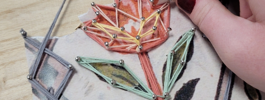 Une main utilise un petit outil pour guider un fil coloré autour de clous sur une planche en bois, créant ainsi une fleur de string art sur un dessin imprimé comme référence - faisant écho aux traditions créatives trouvées au Musée de la Toile de Jouy. - Musée de la Toile de Jouy