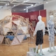 Une salle d'exposition d'art moderne présente des mannequins vêtus de robes à motifs colorés, une structure de dôme géodésique en bois et des œuvres d'art textile exposées sur les murs et les stands. - Musée de la Toile de Jouy
