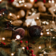 Des ornements de Noël bruns, des branches de pin, des baies rouges et des lumières festives sont disposés sur une surface en bois, évoquant une atmosphère de vacances chaleureuse qui rappelle les charmantes expositions du Musée de la Toile de Jouy. - Musée de la Toile de Jouy