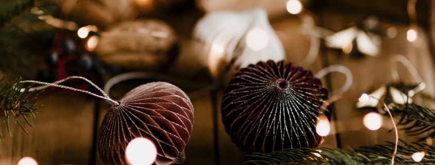 Des ornements de Noël bruns, des branches de pin, des baies rouges et des lumières festives sont disposés sur une surface en bois, évoquant une atmosphère de vacances chaleureuse qui rappelle les charmantes expositions du Musée de la Toile de Jouy. - Musée de la Toile de Jouy
