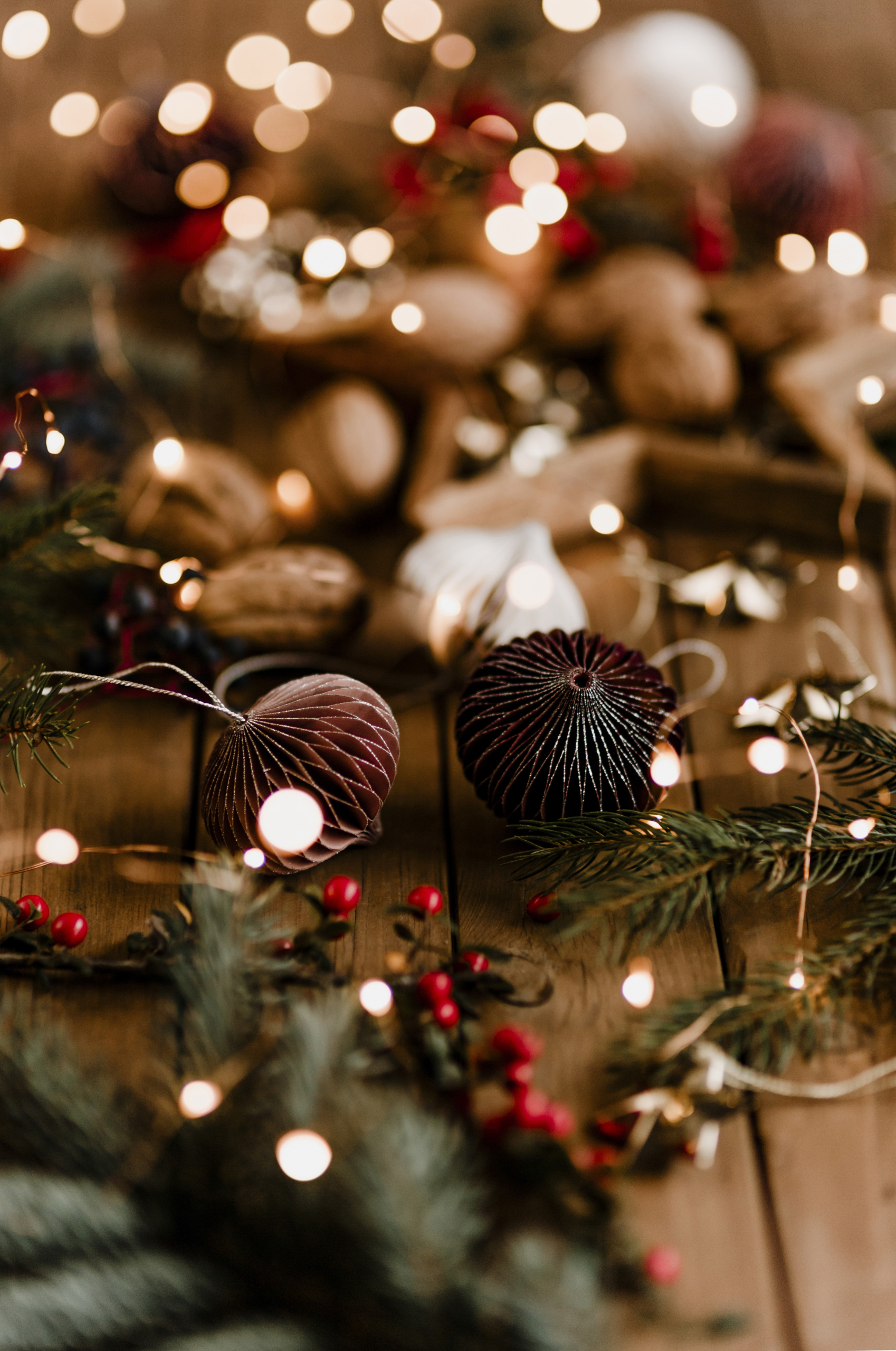 Des ornements de Noël bruns, des branches de pin, des baies rouges et des lumières festives sont disposés sur une surface en bois, évoquant une atmosphère de vacances chaleureuse qui rappelle les charmantes expositions du Musée de la Toile de Jouy. - Musée de la Toile de Jouy
