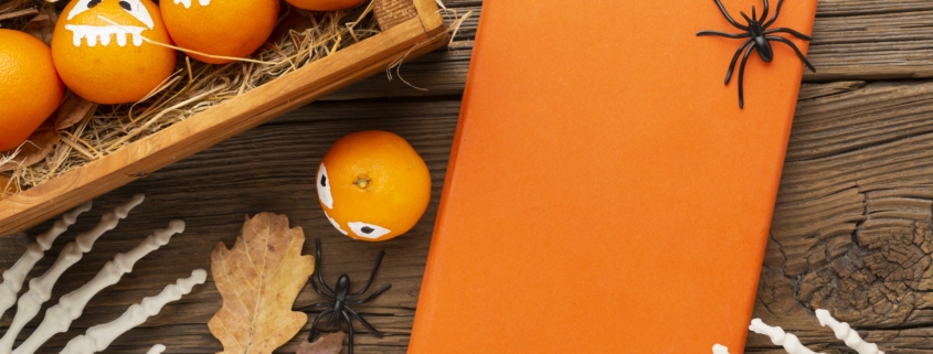 Des oranges avec des visages de lanternes peintes dans une caisse en bois, à côté d'un cadeau enveloppé d'orange avec des araignées jouets, des mains de squelette en plastique et des feuilles d'automne sur une table en bois rustique, évoquent l'esprit festif du Musée de la Toile de Jouy. - Musée de la Toile de Jouy