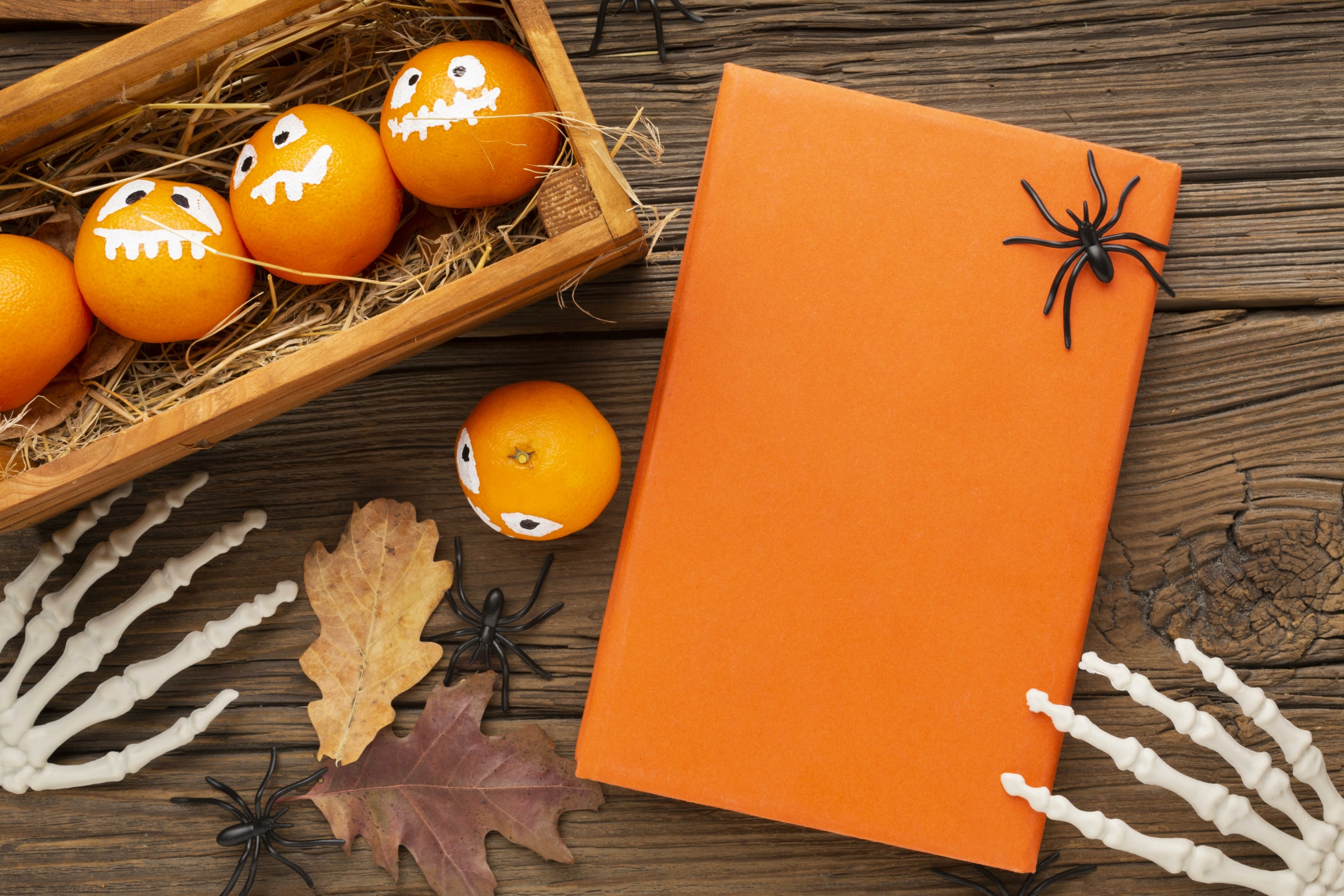 Des oranges avec des visages de lanternes peintes dans une caisse en bois, à côté d'un cadeau enveloppé d'orange avec des araignées jouets, des mains de squelette en plastique et des feuilles d'automne sur une table en bois rustique, évoquent l'esprit festif du Musée de la Toile de Jouy. - Musée de la Toile de Jouy