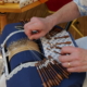 Au musée de la Toile de Jouy, une personne fait de la dentelle avec des fuseaux sur un coussin bleu, en tissant soigneusement des fils. Les mains sont visibles, manipulant habilement les fuseaux en bois pour créer des motifs de dentelle complexes. - Musée de la Toile de Jouy