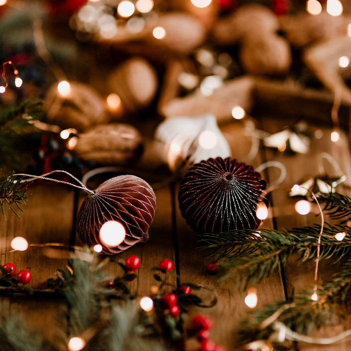 Des décorations de Noël rustiques avec des branches de pin, des baies rouges, des noix et des ornements en papier brun sont éparpillées sur une surface en bois, illuminée par de chaleureuses guirlandes lumineuses - un atelier créatif festif pour célébrer Noël. - Musée de la Toile de Jouy