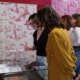 Quatre femmes regardent des documents historiques et des textiles exposés dans une vitrine au Musée de la Toile de Jouy, avec des murs rouges et des panneaux de tissus à motifs en arrière-plan. - Musée de la Toile de Jouy