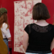 Quatre femmes, dos à la caméra, observent des œuvres d'art textiles à motifs exposées sur des murs rouges dans une galerie du musée de la Toile de Jouy. - Musée de la Toile de Jouy