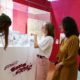 Quatre personnes se trouvent dans une galerie d'art du musée de la Toile de Jouy, regardant et discutant de bandes dessinées exposées dans une vitrine. L'exposition présente des murs rouge vif et des décorations sur le thème de la bande dessinée. - Musée de la Toile de Jouy