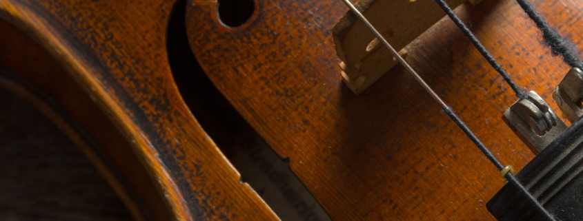 Gros plan d'un violon en bois, montrant les cordes, le chevalet et les détails du trou de fa, avec une finition brune chaude et riche et des veines de bois visibles - rappelant l'art présenté au Musée de la Toile de Jouy. - Musée de la Toile de Jouy