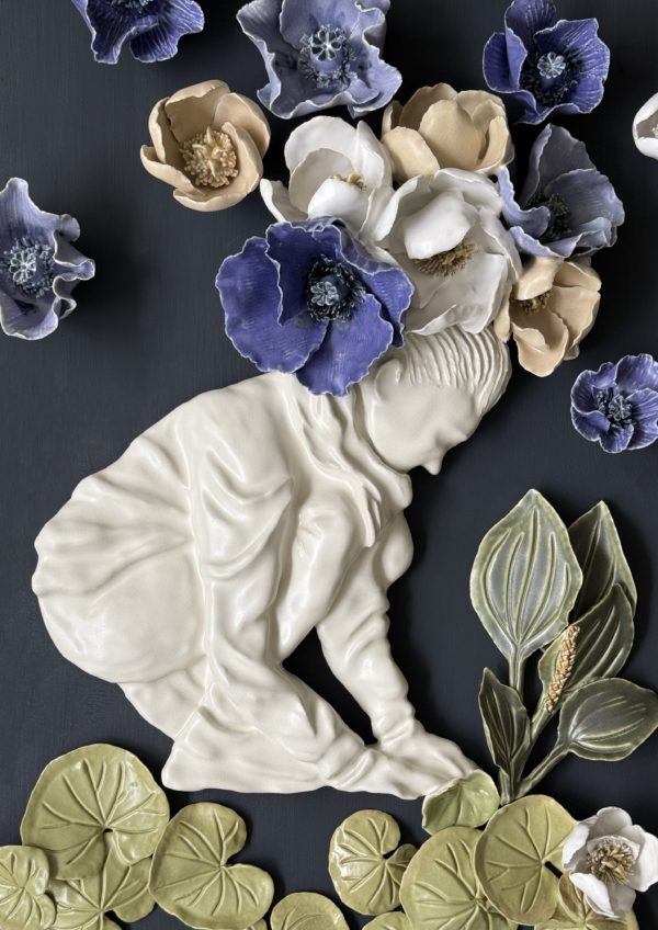 Alice Riehl – Herbarium Interior Preview 01 Œuvre d'art en céramique représentant un enfant agenouillé avec des fleurs s'épanouissant sur sa tête, entouré de feuilles vertes et de fleurs bleues, blanches et beiges sur un fond sombre. - Musée de la Toile de Jouy