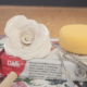 Une rose en argile blanche, fabriquée lors d'un atelier de modelage, est posée sur un bloc rouge de pâte à modeler DAS, avec une éponge jaune, des outils de sculpture et un tapis à motifs floraux à côté, le tout posé sur un sol en bois et un mur uni. - Musée de la Toile de Jouy