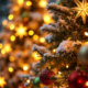Gros plan sur un sapin de Noël saupoudré de neige, orné de décorations dorées et rouges et de lumières scintillantes, évoquant la magie d'un « Atelier créatif Noël » pendant les vacances de Noël pour les enfants de 7 à 12 ans, avec un autre sapin illuminé flou en arrière-plan. - Musée de la Toile de Jouy