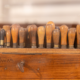 Une rangée d’outils à manche en bois, sans doute des ciseaux ou des outils de sculpture, est soigneusement disposée à la verticale dans un support en bois posé sur un établi, ce qui rappelle la présentation soignée que l’on retrouve dans les collections permanentes des musées. - Musée de la Toile de Jouy