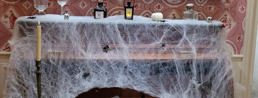 Un bureau recouvert de fausses toiles d'araignées, agrémenté d'araignées, de bougies, de crânes, d'une lanterne, d'une citrouille blanche et de lettres manuscrites, crée une ambiance effrayante d'Halloween qui rappelle un atelier créatif — une source d'inspiration idéale pour les fêtes de la Toussaint. - Musée de la Toile de Jouy