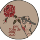 Une main recouverte d'un tissu à motifs floraux tient une rose sur un fond beige rond, soulignant avec élégance l'esprit du Prix Toile de Jouy 2027. Le texte « Prix Toile de Jouy 2027 » est inscrit en rouge. - Musée de la Toile de Jouy