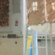 Une femme vêtue d'une salopette en jean observe une petite cabane en bois surélevée, issue du spectacle « Cabane » de la Compagnie les Eduls. - Musée de la Toile de Jouy